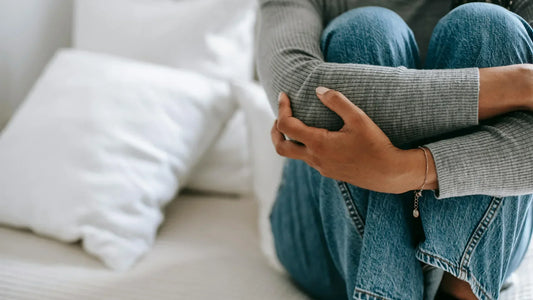 anxious woman sitting on bed with arms wrapped around knees